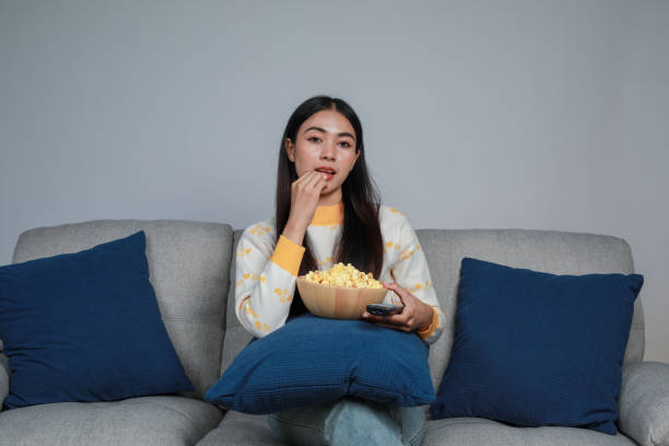 istock Young woman sitting on sofa while watching TV with popcorn in the room 1666571005