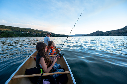 Family living an active lifestyle outdoors. Mother fishing and canoeing with her daughters.