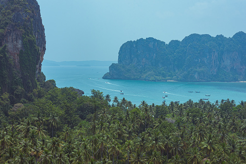 Rocks and coconut tree groves of Railay Peninsula, a view from Railay Viewpoint, as well as long-tail boats going from Ao Nang to Railay West Beach and back.