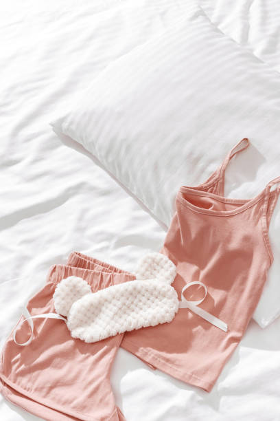 ベッドの上にピンクの女性のパジャマとふわふわの睡眠アイマスク。寝るためのトップビューの夏のパジャマ。審美的なライフスタイルフラットレイ写真、シングレットとショートパンツの� - homewares cushion fake fur blanket ストックフォトと画像