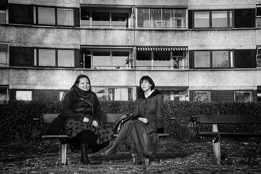 Two womens sitting on a bench in front of a building