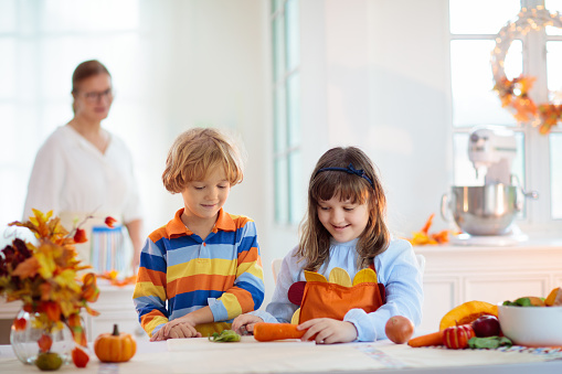 Family cooking Thanksgiving dinner. Grandmother and child cut pumpkin in decorated kitchen. Mother and kid cook vegetable meal in autumn. Grandparents visit. Fall season food.