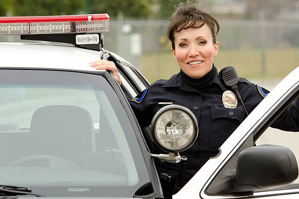smiling officer A Hispanic female police officer smiles while standing next to her patrol car. police force smiling officer stock pictures, royalty-free photos & images