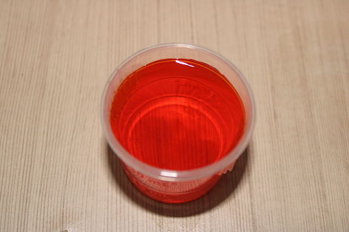Closeup of orange-colored cold medicine in a dosage cup