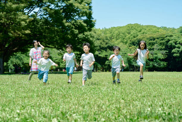 Children running and a woman watching Children running and a woman watching in the park japanese boy and girl stock pictures, royalty-free photos & images