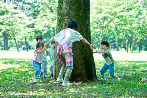 Children and woman holding hands and going around the tree in the park