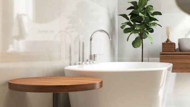 Round wooden side table, bathtub, fiddle leaf fig tree in luxury design bathroom in sunlight on white tile wall