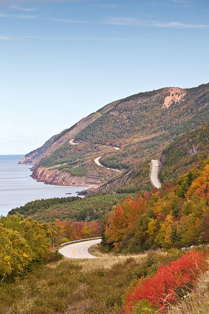 Scenic Highway Along The Sea A highway through a colourful forest along the sea. Cabot Trail. Nova Scotia, Cape Breton, Canada. Fall scenic. Vertical colour image. cabot trail stock pictures, royalty-free photos & images