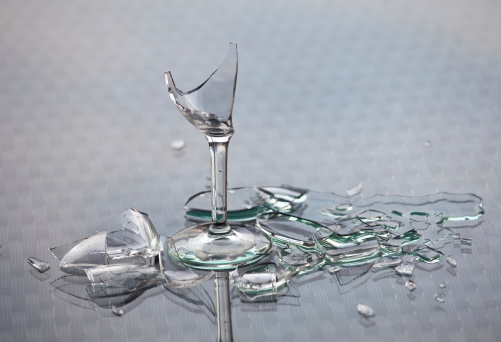 A concept image of a spilled alcoholic drink and broken glass. Themes of the image include alcoholism, drinking, binge drinking, addiction, beverage, glass, broken, smashed, wine glass, busted, shattered, sharp, spilled, mess, cleanup, concept image of alcohol abuse. 