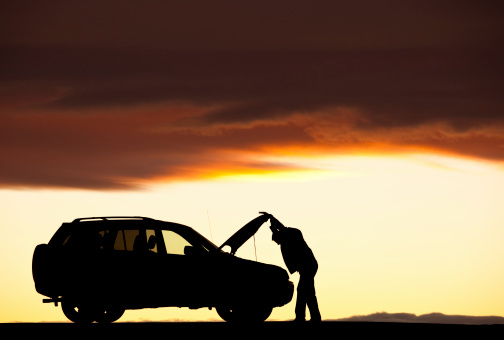 A silhouette of a man beside his vehicle having mechanical difficulty. SUV. Roadside assistance needed. Car trouble. Horizontal colour image. Rural highway.