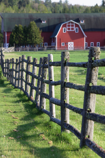 A rural, rustic wooden fence covered with patches of moss and a large red barn casting late afternoon shadows. Located near the town of Lake Placid in upstate New York.