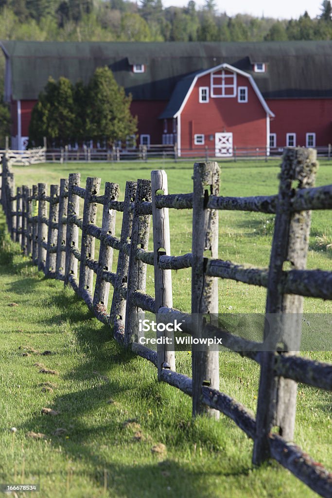 Rustic Wooden Fence and Distant Red Barn A rural, rustic wooden fence covered with patches of moss and a large red barn casting late afternoon shadows. Located near the town of Lake Placid in upstate New York. Agricultural Building Stock Photo