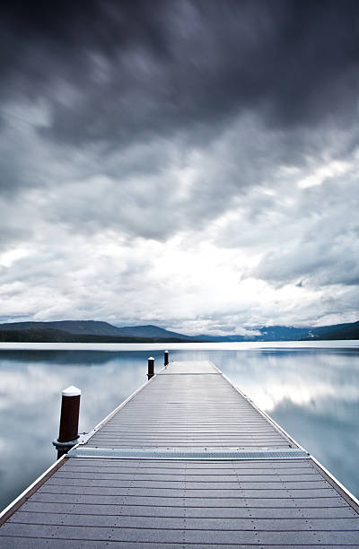 A dock on a mountain lake. Near Whitefish, Montana, United States. Moody sky. Vertical landscape. Additional themes include nature, water, lakes, scenic, dramatic, Montana, raw, rugged, storm, stormy, thunderstorm, serene, quiet, still, nobody, and Going to the sun road. 