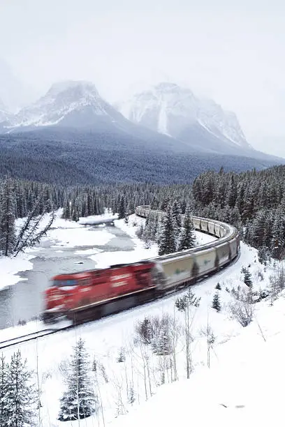 Photo of Red Train Speeding Through Rocky Mountains