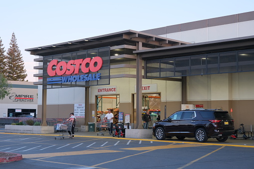 Rancho Cordova, California, USA - April 11, 2023: Late evening shot of people walking in and out of a Costco Wholesale warehouse in Rancho Cordova. Costco Wholesale operates an international chain of membership warehouses, carrying brand name merchandise at substantially lower prices.