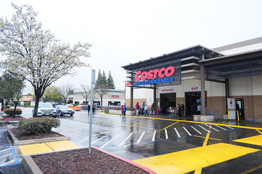 Rancho Cordova, California, USA - March 19, 2023: Late evening shot of people walking in and out of a Costco Wholesale warehouse in Rancho Cordova. Costco Wholesale operates an international chain of membership warehouses, carrying brand name merchandise at substantially lower prices.