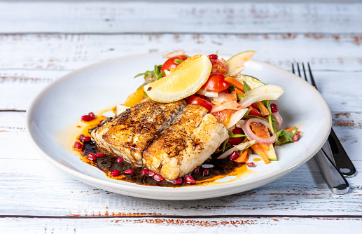 Grilled Barramundi with a side of salad, served on a white round plate with knife and fork.
