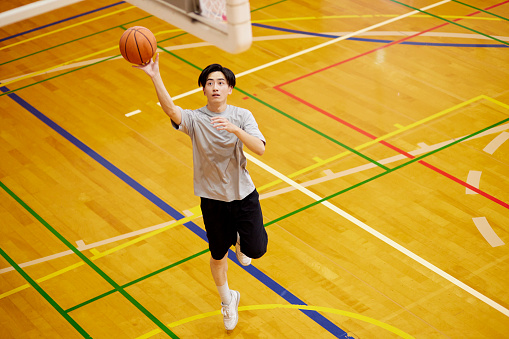 Japanese male university student practicing basketball in the gymnasium