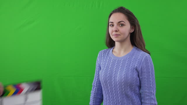 Clapperboard in male Caucasian hands clipping leaving and young woman looking at camera. Portrait of talented beautiful actress posing at green screen chromakey background.