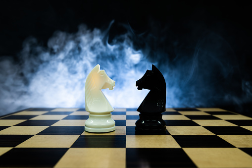 Two chess knights in fog on black background.