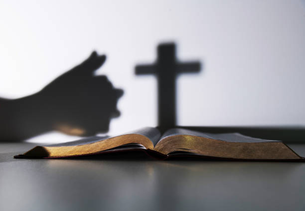 Silhouette of human hand praying with a cross.