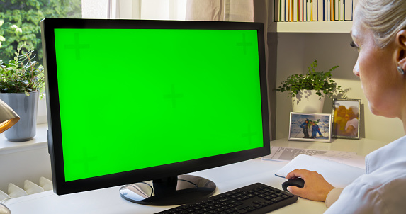 Woman using green screen of computer monitor in home office.