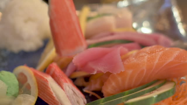 Closeup of sushi sashimi plate in restaurant. Piece picked up with chopsticks.