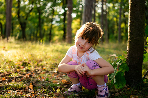 A cute little girl is sitting in nature on a summer day and looking at the camera