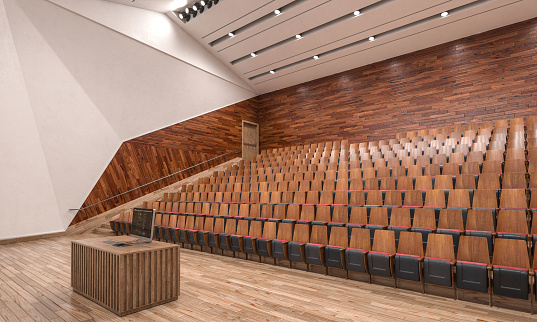 Empty auditorium at university with wooden chairs and banks and large windows and stairs on one side. The chairs are arranged in rows and their backrests form a pattern.