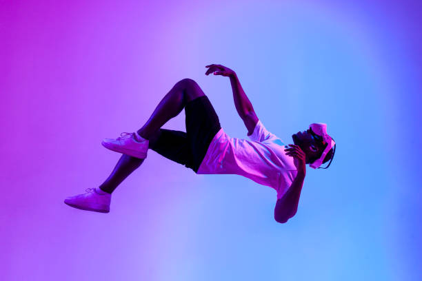 african american male gamer in virtual reality glasses flies in the air and falls in neon lighting, guy plays with vr african american male gamer in virtual reality glasses flies in the air and falls in neon lighting, guy plays with vr gadget and levitates, concept of imagination and fantasy levitation stock pictures, royalty-free photos & images