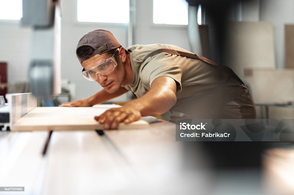 Junger Schreiner, der ein Stück Holz mit einer Kreissäge in einer Möbelfabrik schneidet - Lizenzfrei Schreiner Stock-Foto Junger Schreiner, der ein Stück Holz mit einer Kreissäge in einer Möbelfabrik schneidet - Lizenzfrei Schreiner Stock-Foto