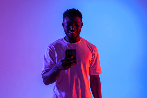 istock african american man is using smartphone and smiling in neon lighting, guy is typing on phone online 1667131482