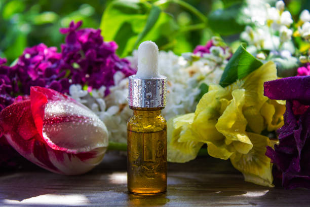 An amber glass bottle used for aromatherapy placed outdoors next to a yellow autumn leaf on a mossy surface