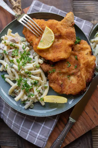 Delicious german comfort food with fresh pan fried and breaded pork cutlets. Served with homemade noodle salad on a plate on rustic and wooden table background. Top view, closeup