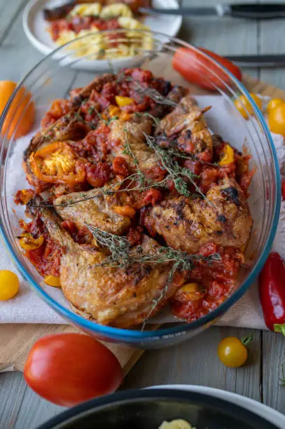 Delicious homemade roasted chicken legs with braised tomato ragout and italian herbs. Served ready to eat in a casserole dish on a table.