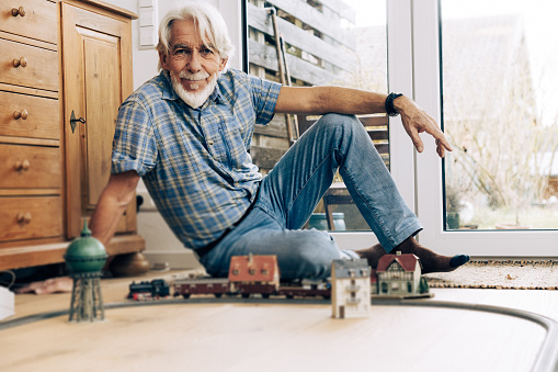 Indoor portrait of senior man playing with model steam train in his living room.