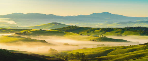 house surrounded by cypress trees among the misty morning sun-drenched hills of the val d'orcia valley at sunrise in san quirico d'orcia, tuscany, italy - val tuscany cypress tree italy imagens e fotografias de stock