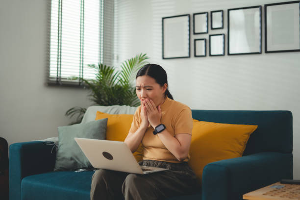 istock Asian woman sitting at home using laptop, feels concerned thinking about work. 1667195390
