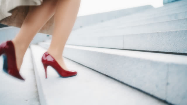 SLO MO An elegantly dressed, unrecognizable woman in red stilettos walks up the stairs in front of a modern building