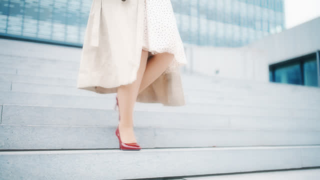 SLO MO An elegantly dressed, unrecognizable woman in red stilettos walks down the stairs in front of a modern building