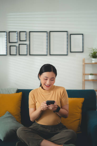istock Asian woman happy smiling sitting on sofa and using smart phone at home. 1667215899
