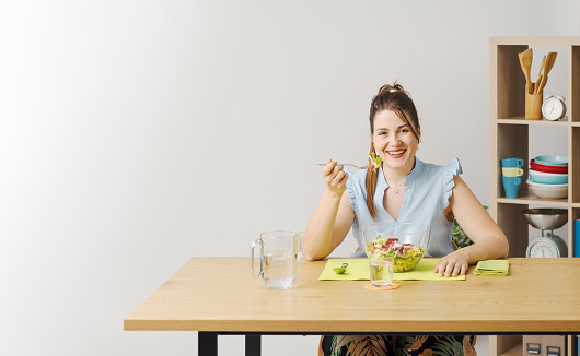 Happy young woman sitting and having a healthy lunch break, she is eating fresh salad, diet and nutrition concept