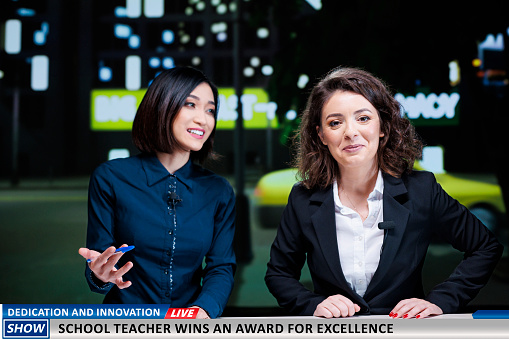 Genious teacher winning award for showing innovation in education system, diverse presenters talk about huge achievement on live television channel. Newscasters team reveal success of professor.