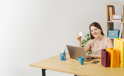 Happy woman sitting at the desk and doing online shopping with her laptop, business and commerce concept