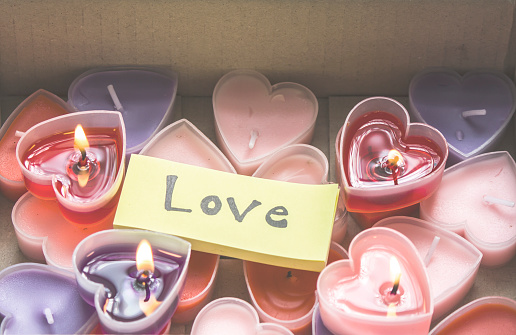 Lots of heart-shaped candles are in a Valentine's Day gift box with yellow paper and love messages.