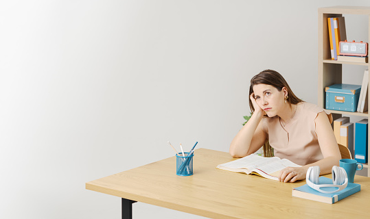 Tired woman sitting at the desk and studying, she is disappointed and pensive