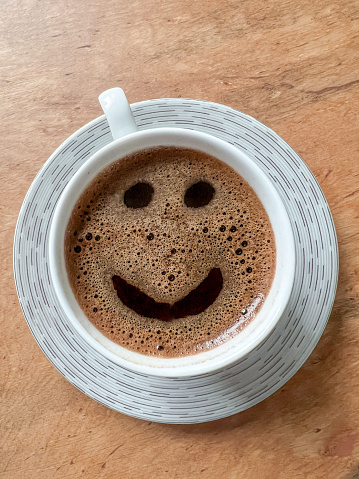 coffee, top view beautiful cup of greek or turkish coffee with smile face icon on wooden table or background. happy or funny moments in a cafe. hot drink or beverage concept with smiling face icon