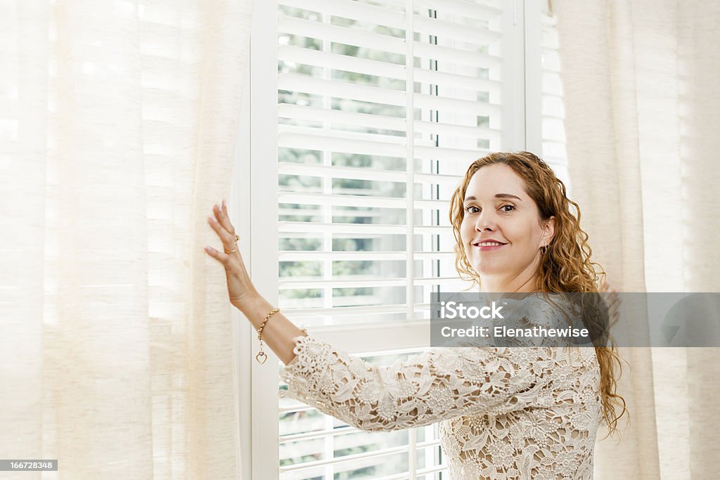 Donna sorridente vicino alla finestra - Foto stock royalty-free di Persiana - Caratteristica architettonica