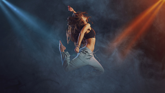 Professional female dancer performing on stage, she is jumping surrounded by smoke, dance and entertainment concept