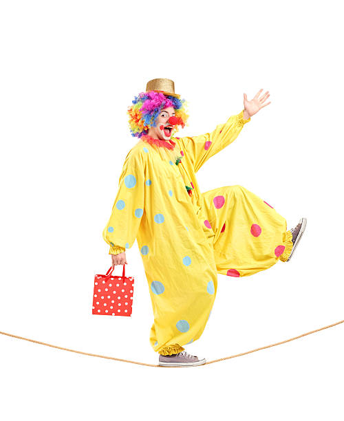 Full length portrait of a clown holding a bag and walking on a rope isolated on white background